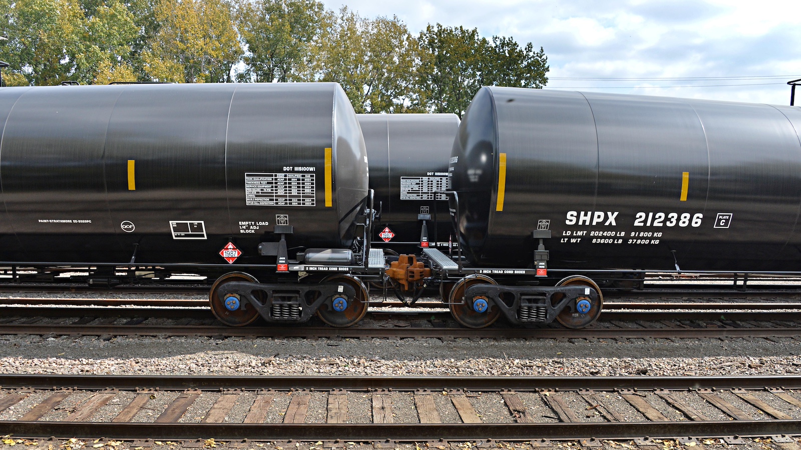 Two black cylindrical rail cars are hitched to each other, with a third in the background and an empty railroad track in the foreground