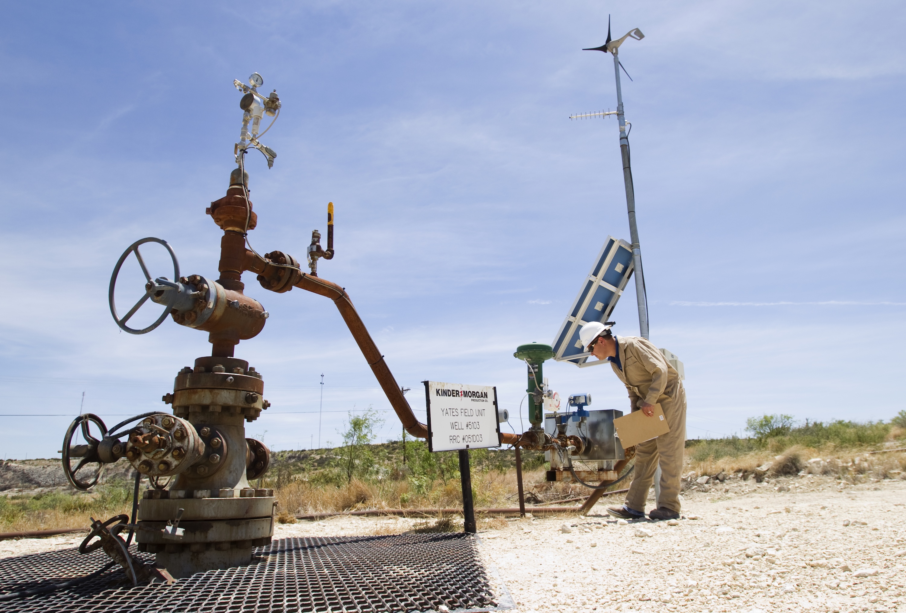A person stands on a dirt road and inspects a rusty carbon capture well