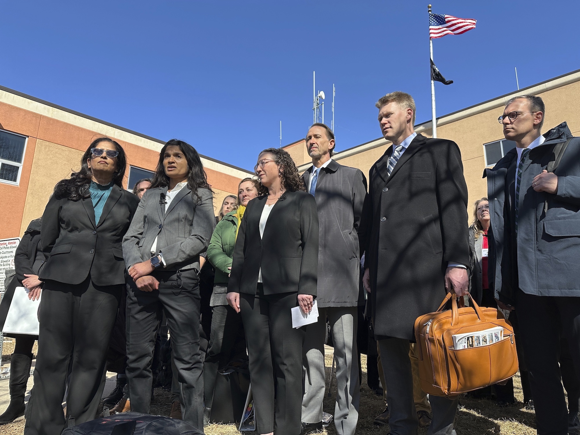 A group of people in suits stand outside a courthouse