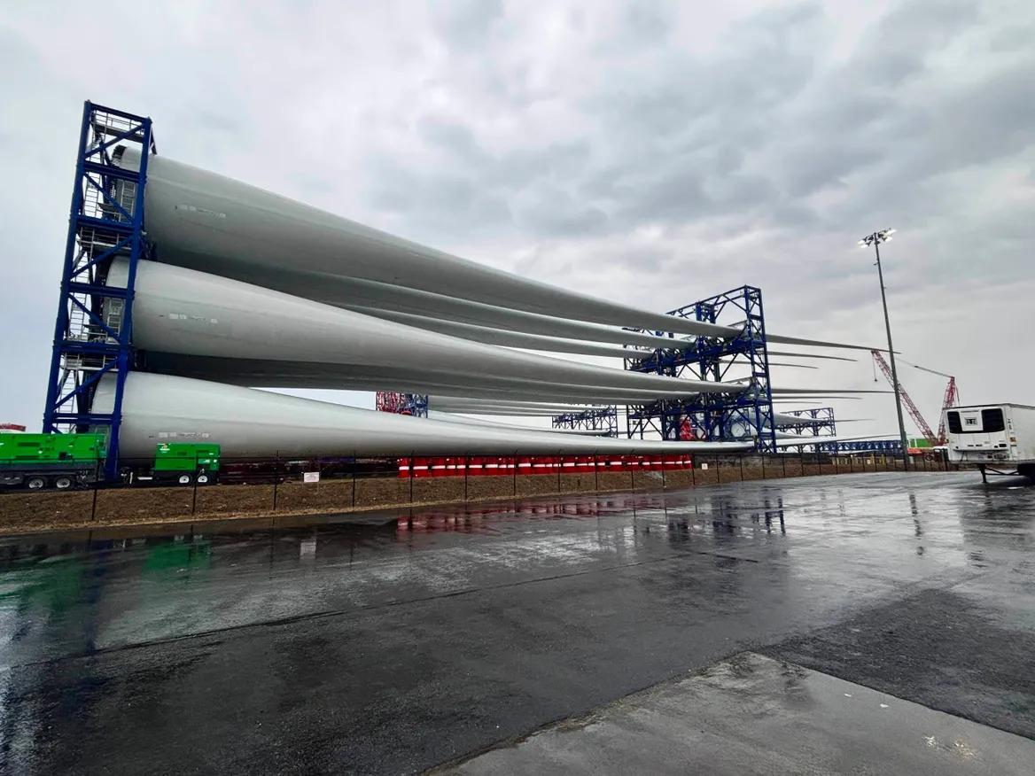 Massive white wings of wind turbines sit in a port