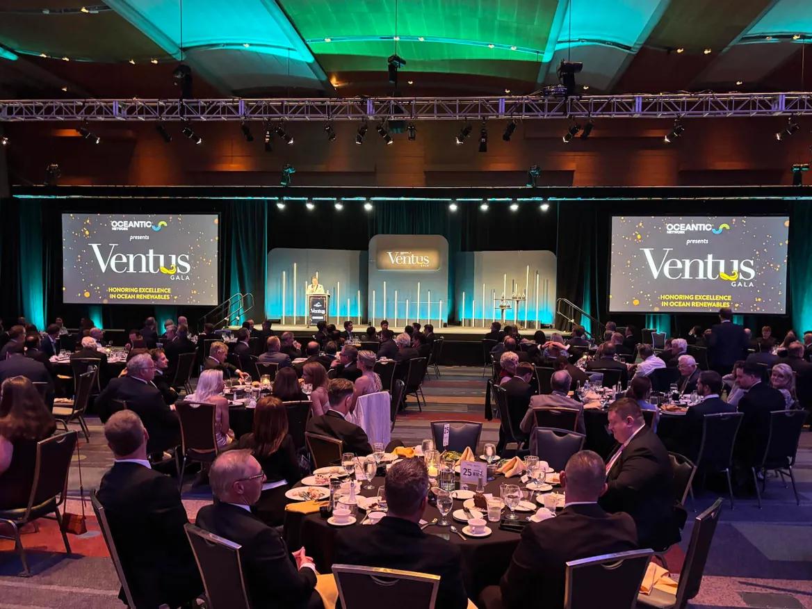 People are seated at banquet tables in front of a stage