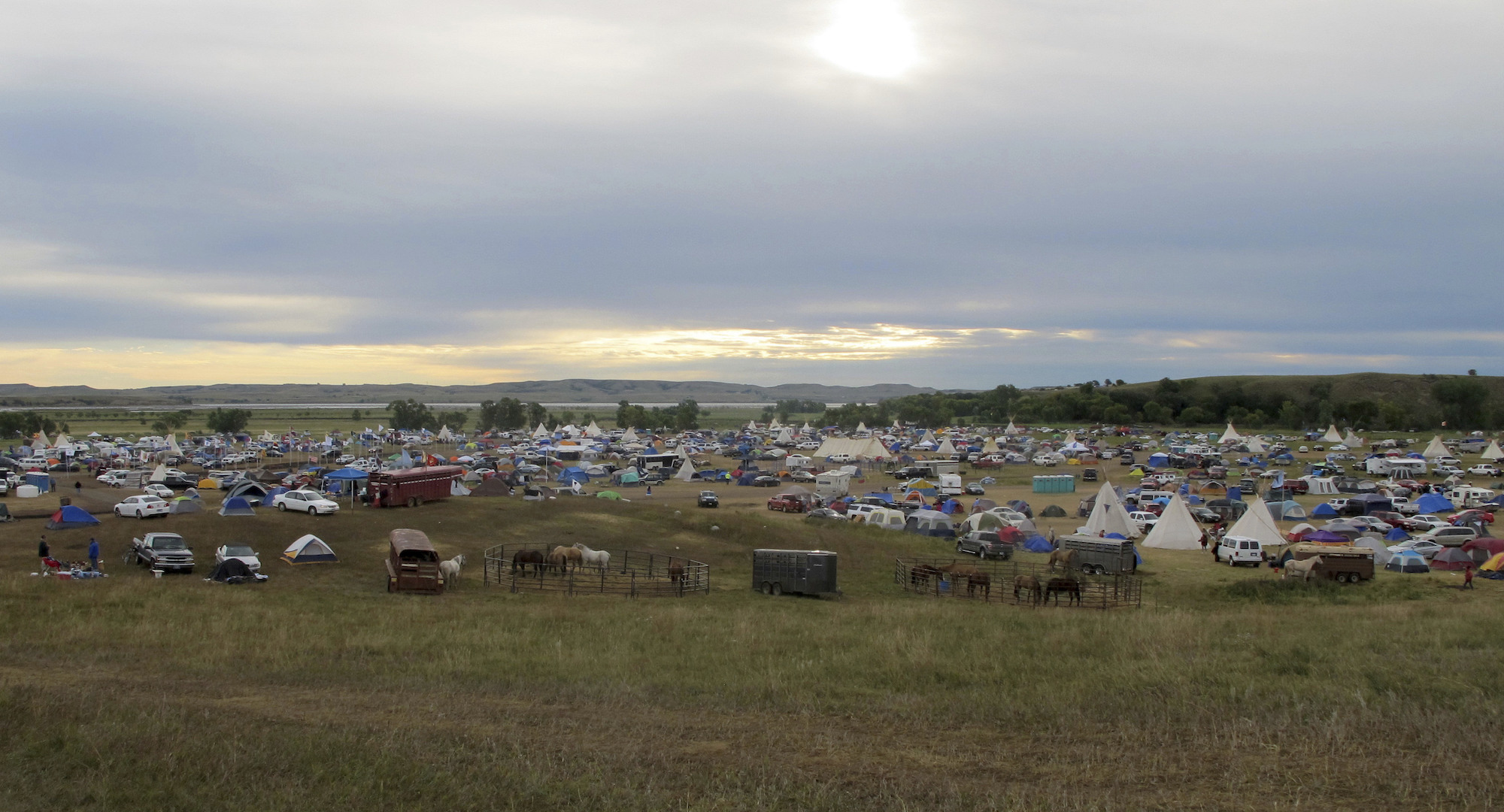 A large camp on a grassy field with tents, teepees, and other structures