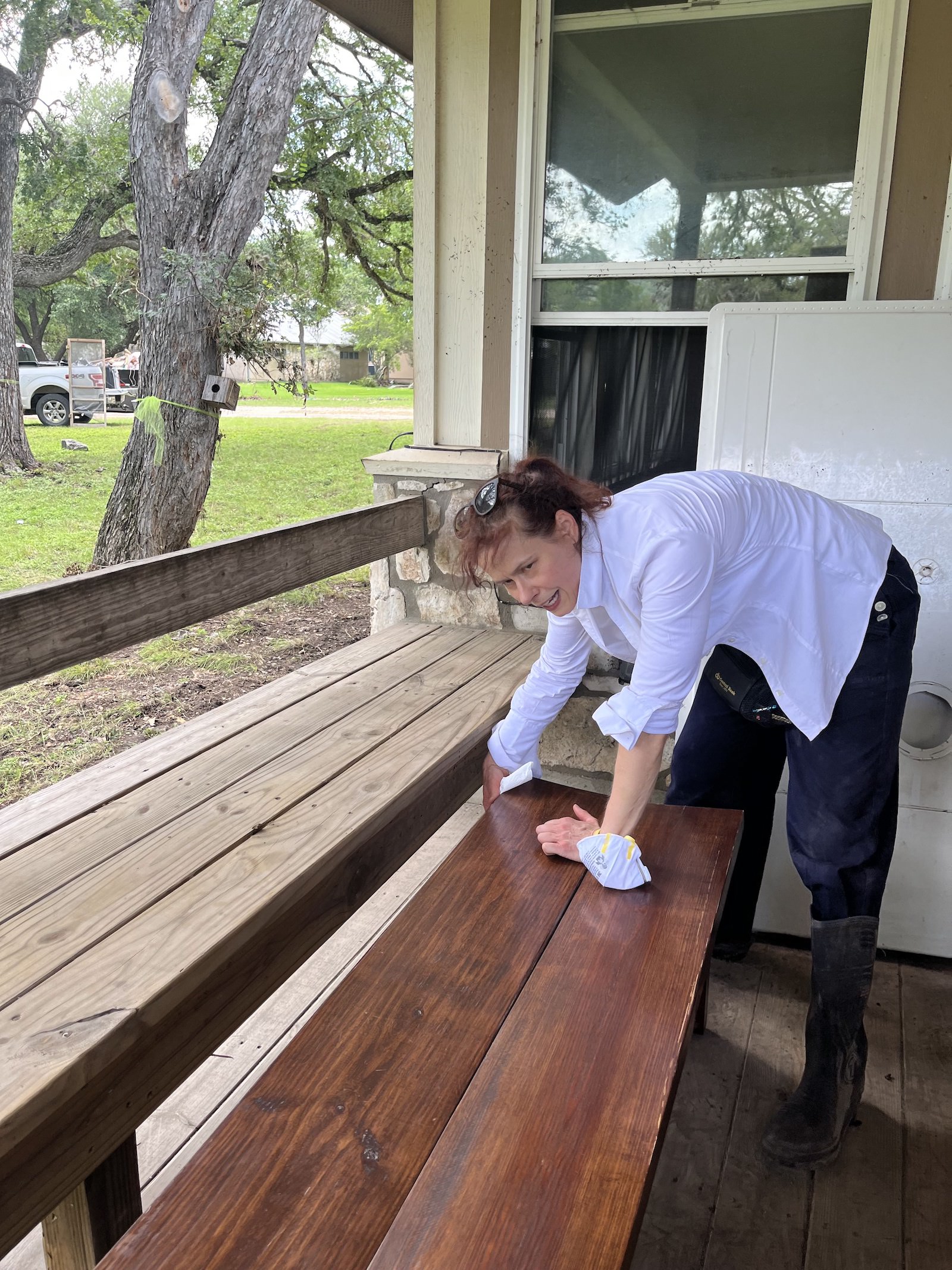 a woman leans over a heavy wooden bench on a porch